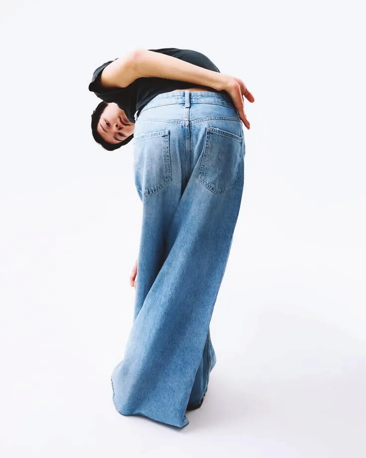 Model bent forward in light-wash wide-leg jeans that pool at the floor